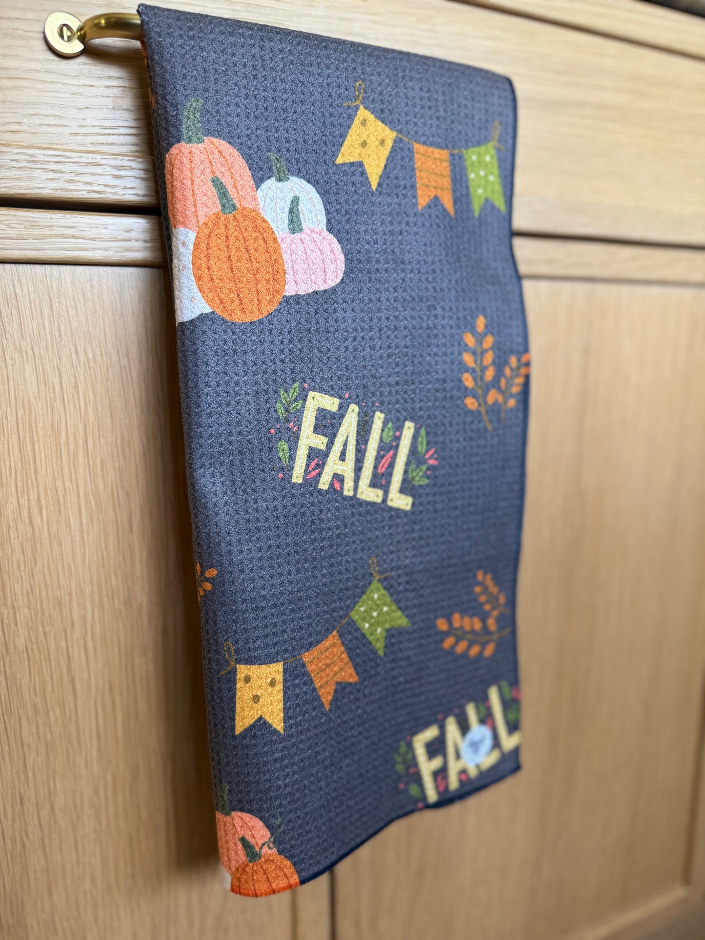 fall themed dishtowel folded over a gold drawer pull