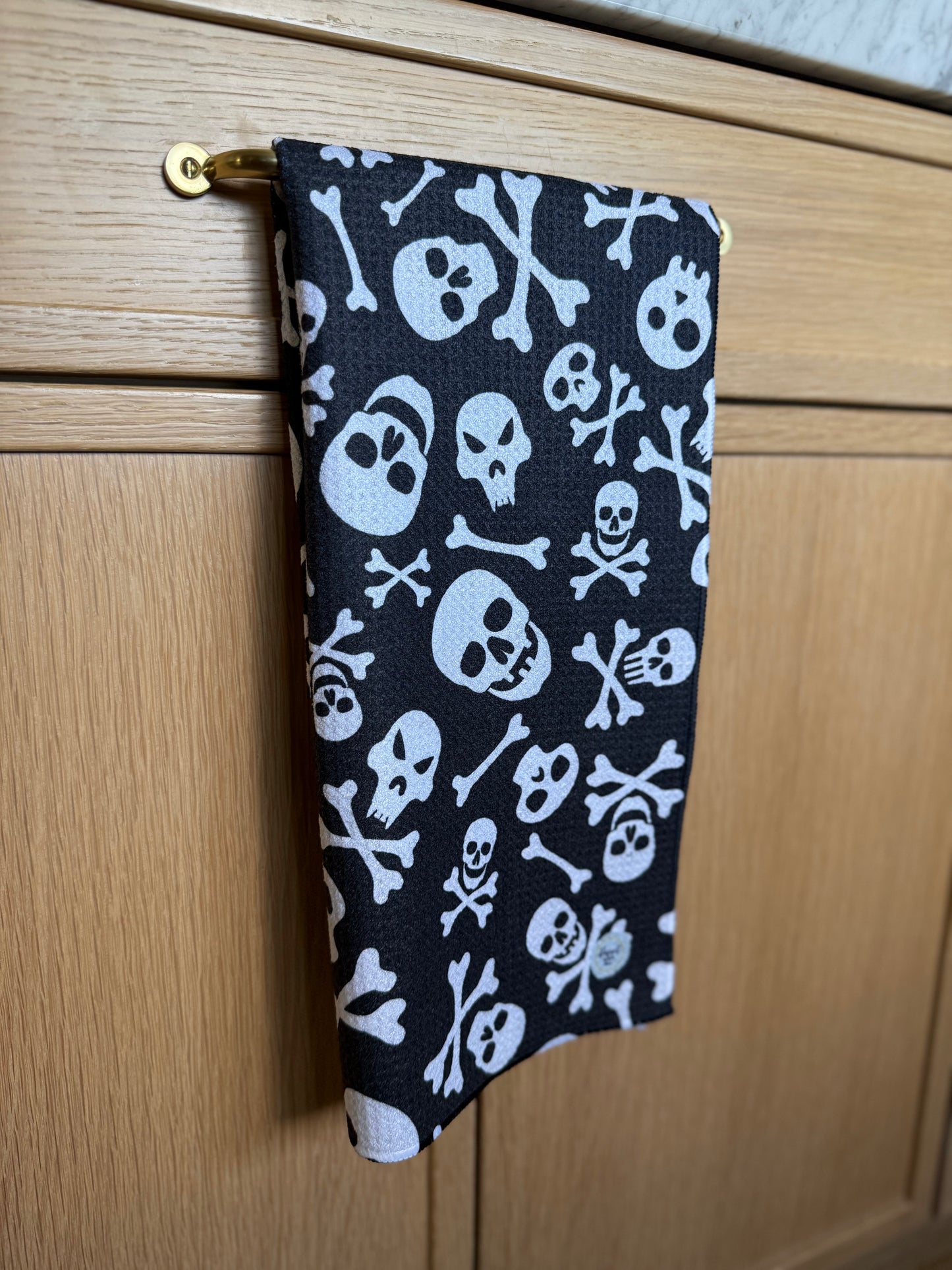 Black towel with white skull and crossbones pattern hanging on a wooden cabinet.