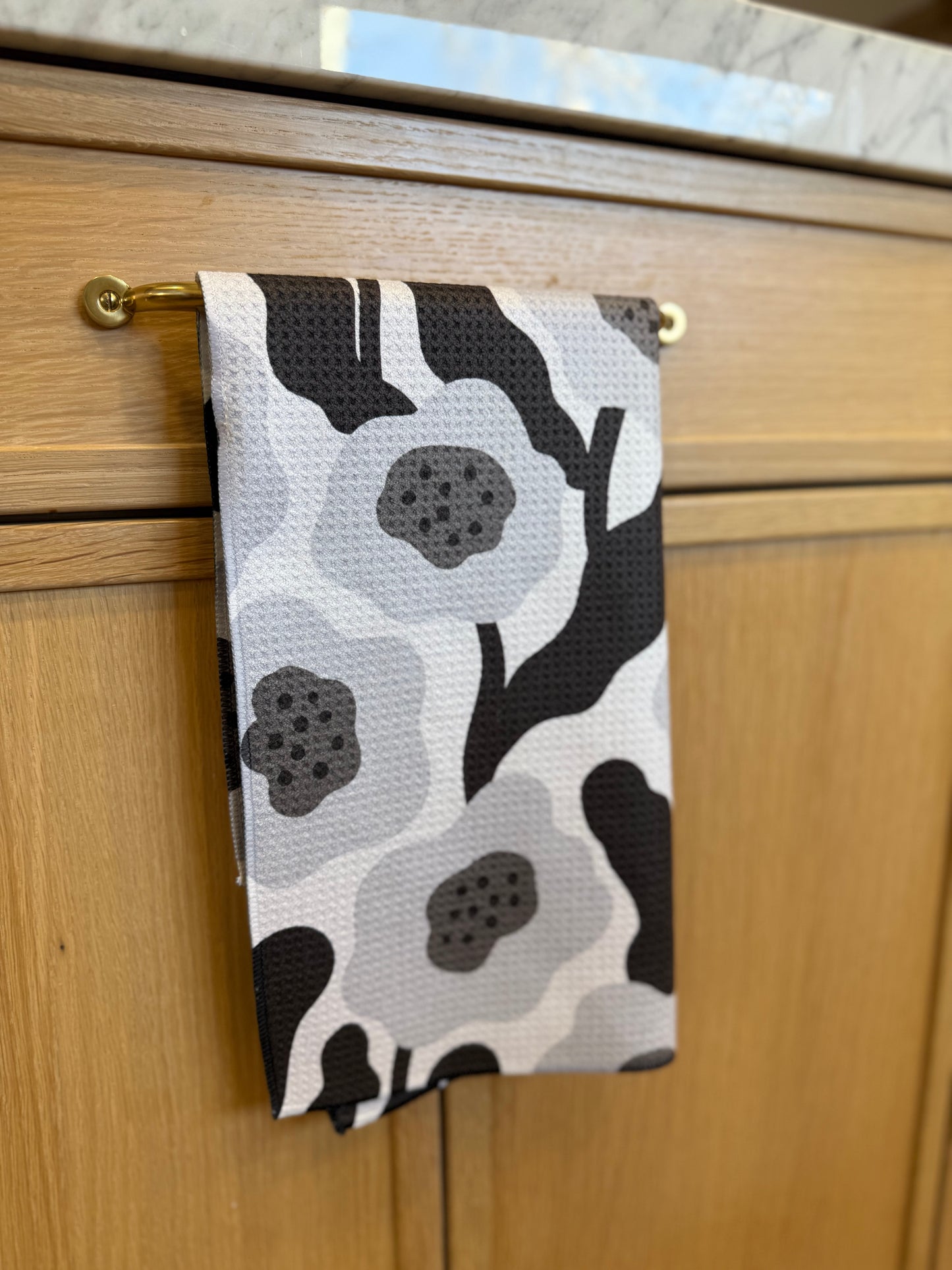 Black and white floral patterned towel hanging on a wooden cabinet handle.
