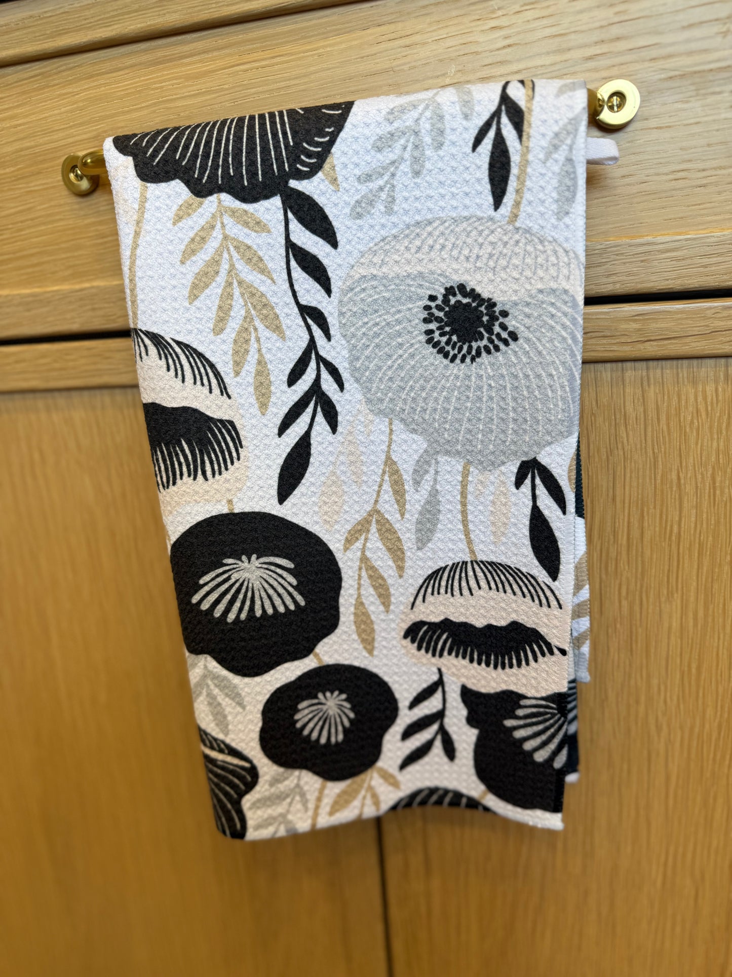 Floral patterned towel hanging on a wooden cabinet with gold knobs.
