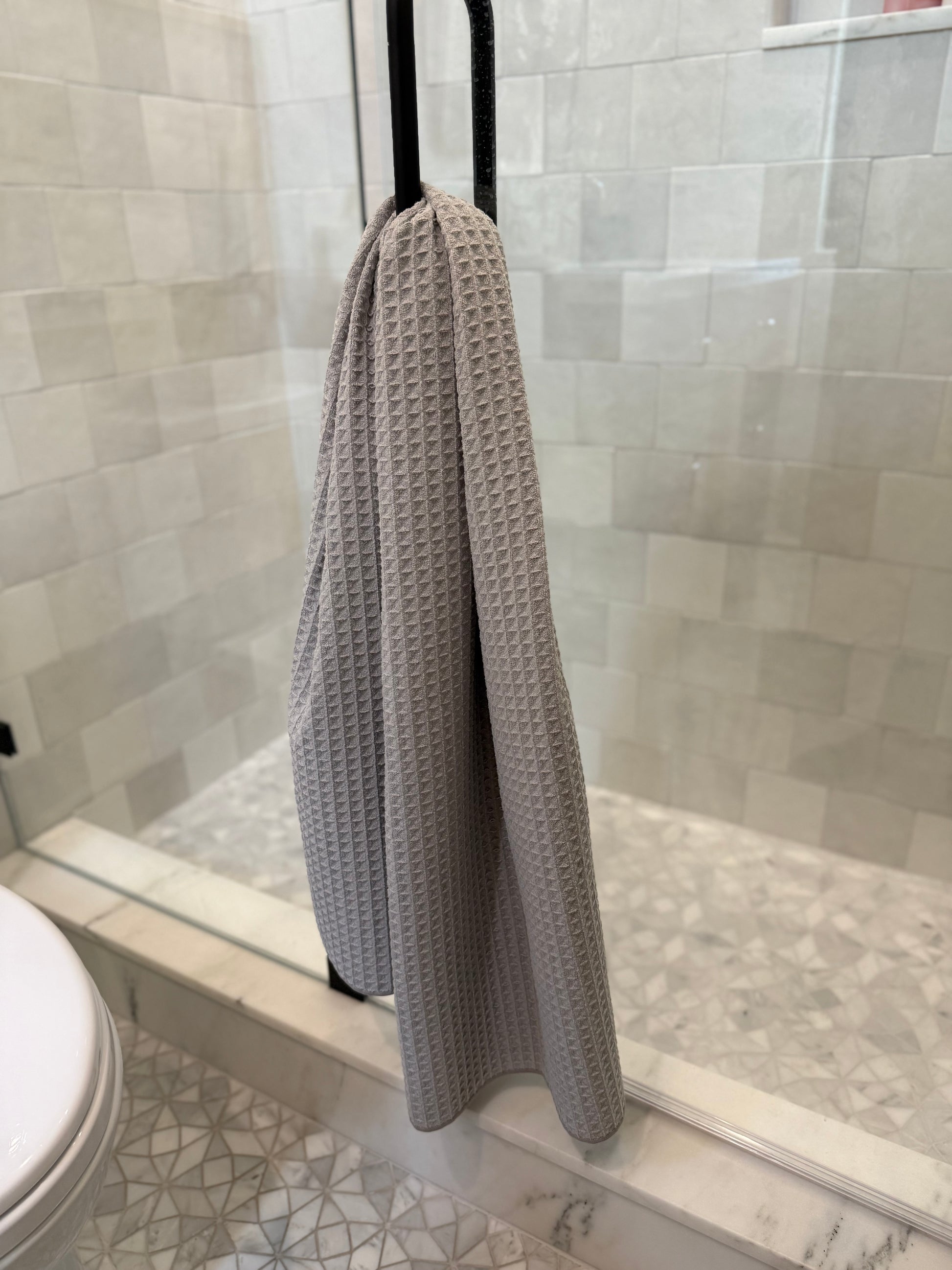 Gray textured towel hanging on a shower door in a tiled bathroom.