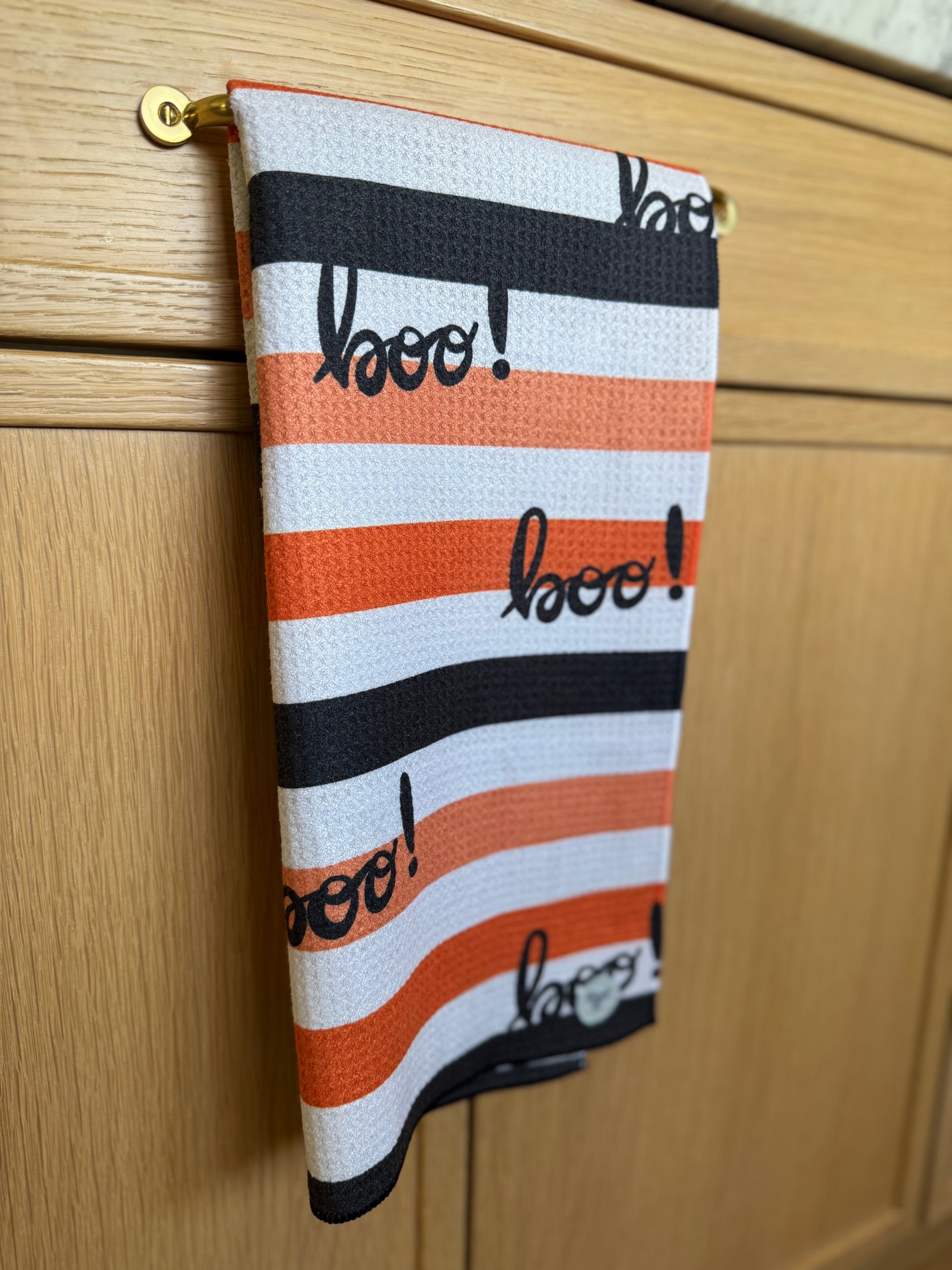 Striped towel with 'boo!' text hanging on a wooden cabinet.
