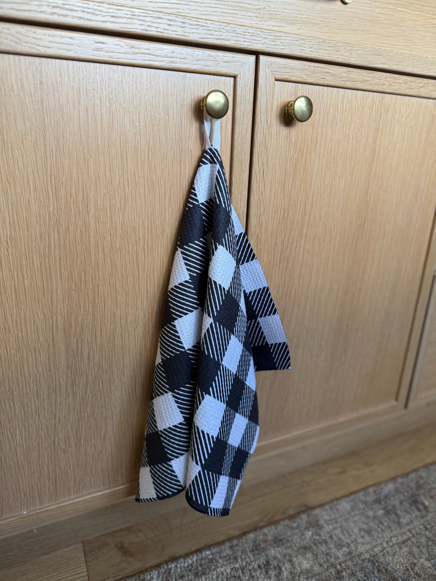Black and white checkered towel hanging on a wooden cabinet door with hanging loop
