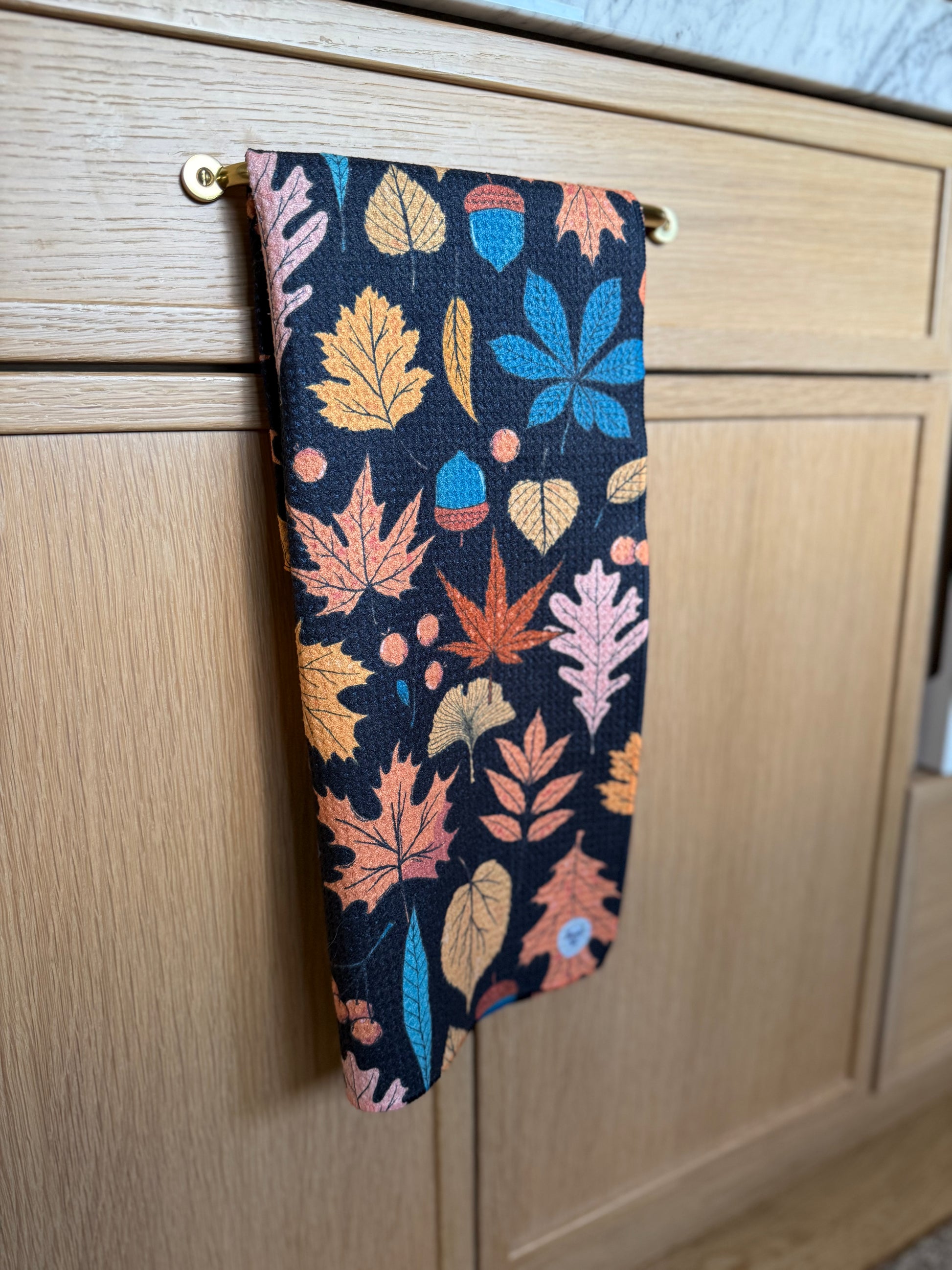 Decorative kitchen towel with leaf pattern hanging on a wooden cabinet.