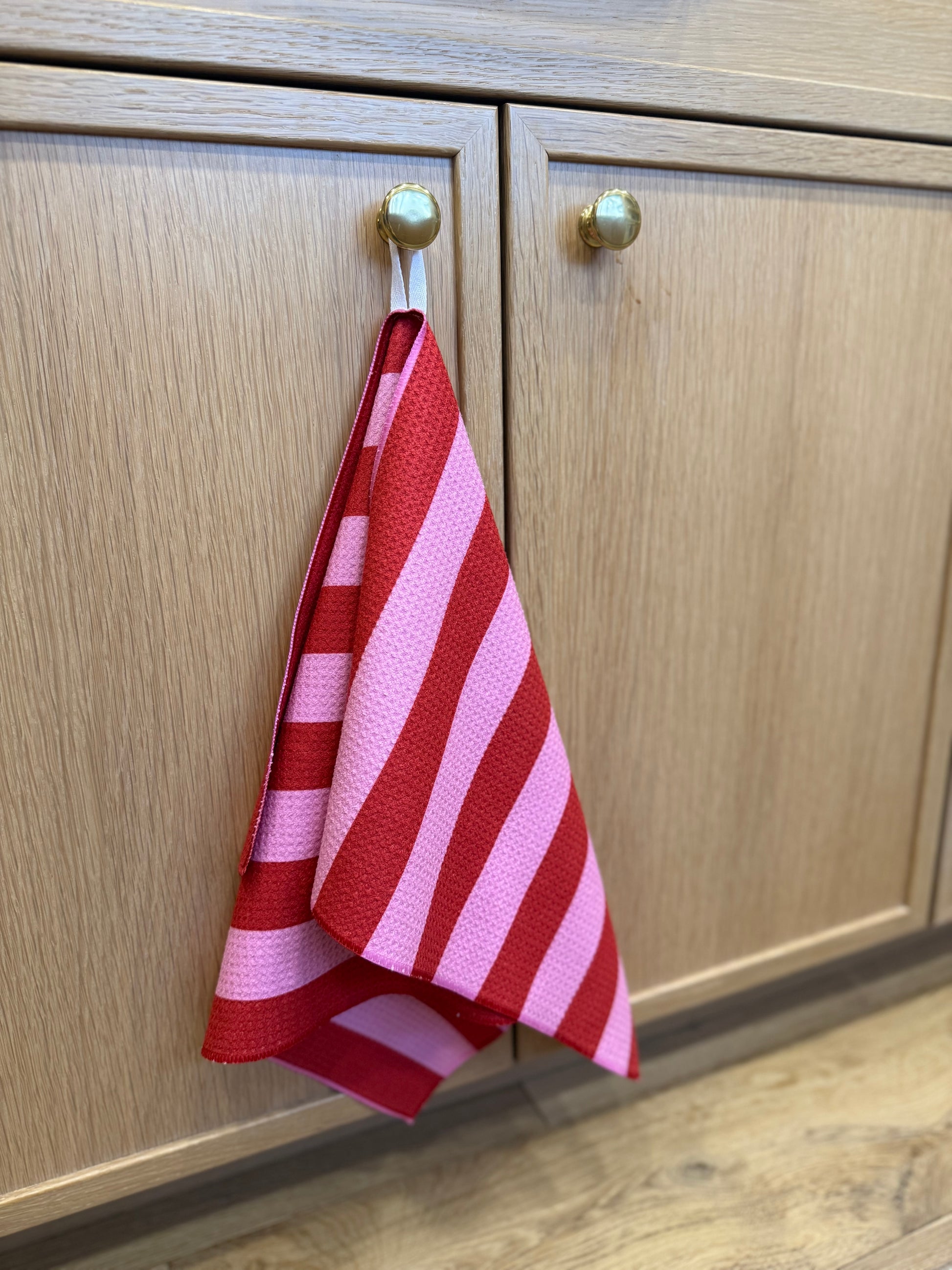 Red and pink striped towel hanging on a wooden cabinet door.