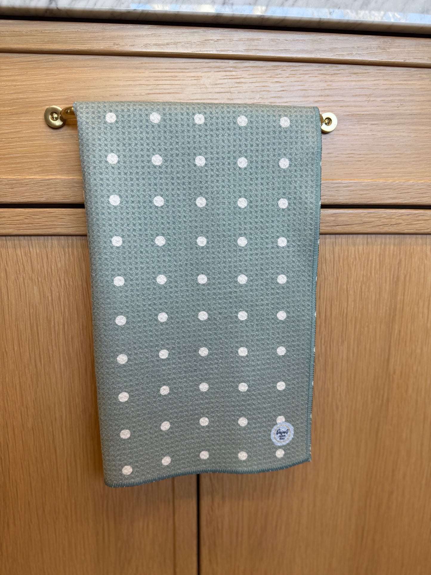 Green towel with white polka dots hanging on a wooden cabinet.