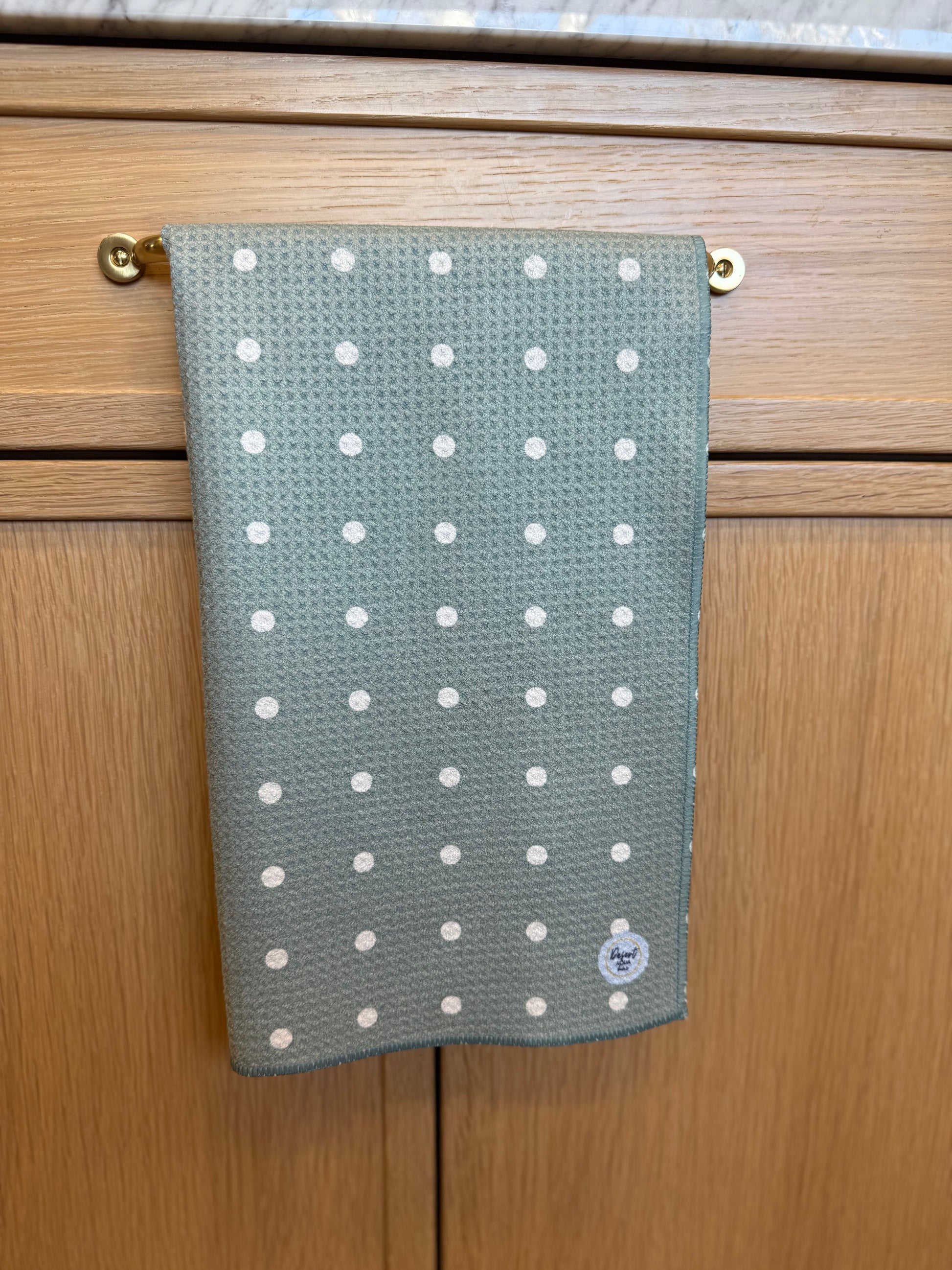 Green towel with white polka dots hanging on a wooden cabinet.