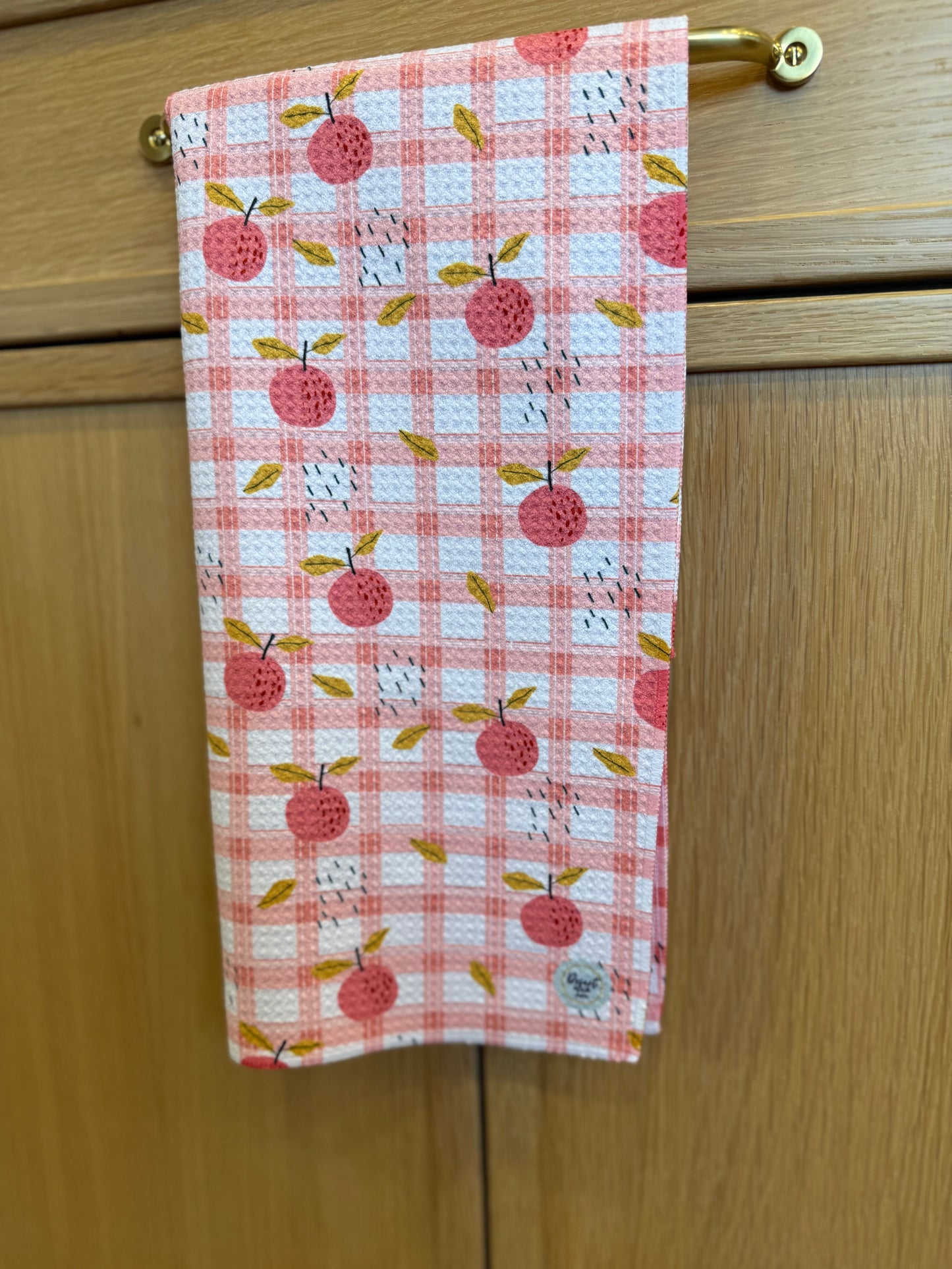 Checkered towel PEACH pattern hanging on a wooden cabinet.