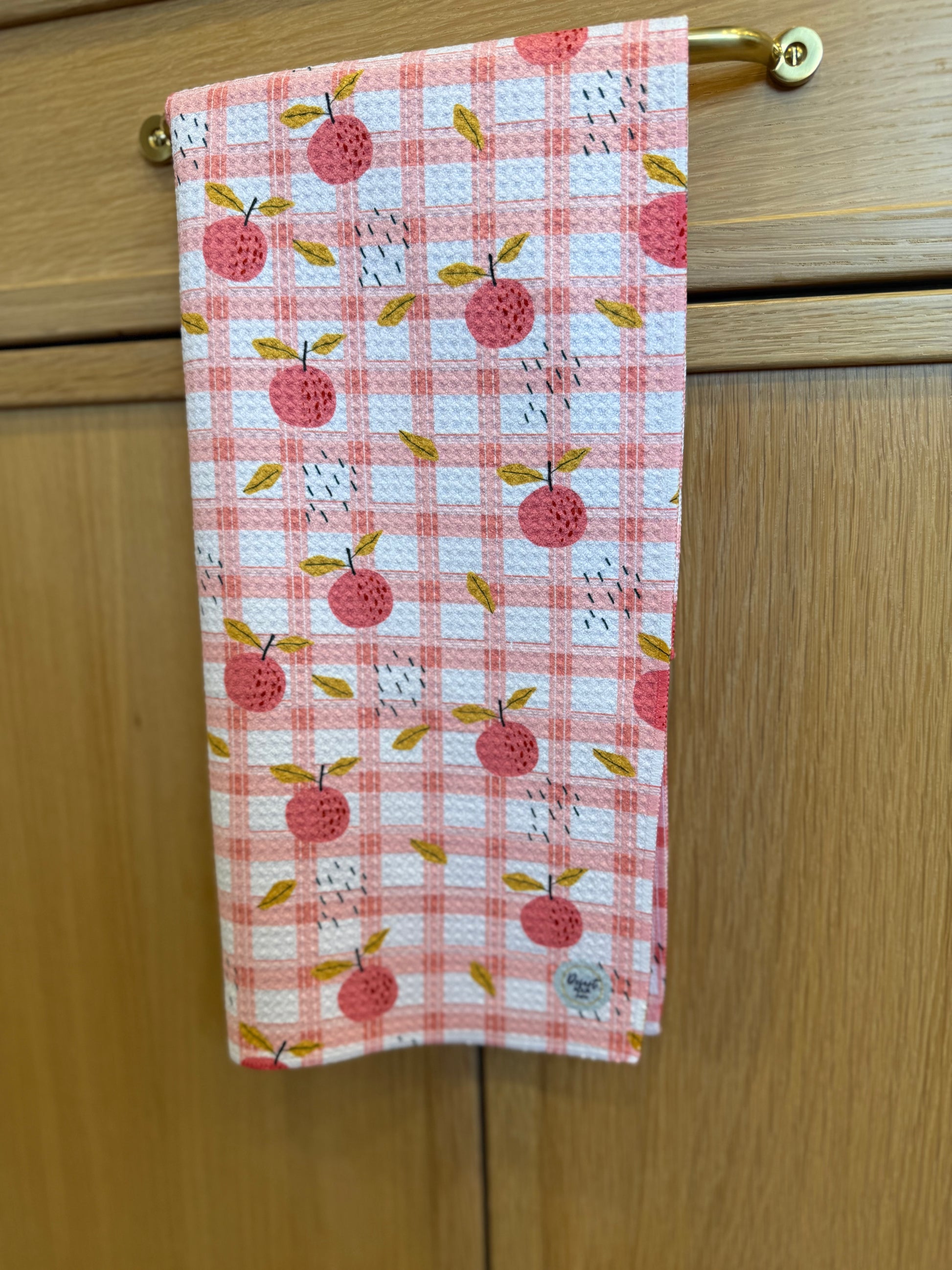 Checkered towel PEACH pattern hanging on a wooden cabinet.