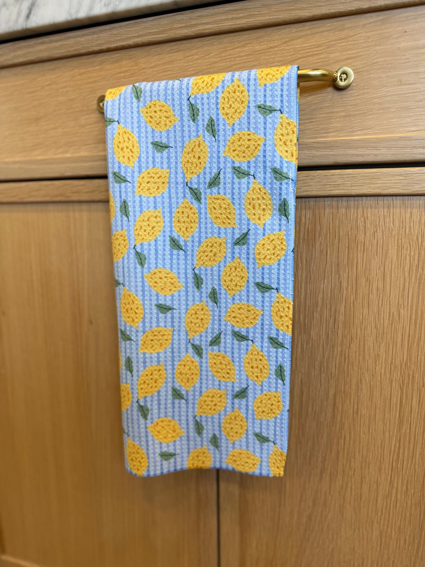 Towel with yellow LEMON  pattern hanging on a wooden cabinet handle.